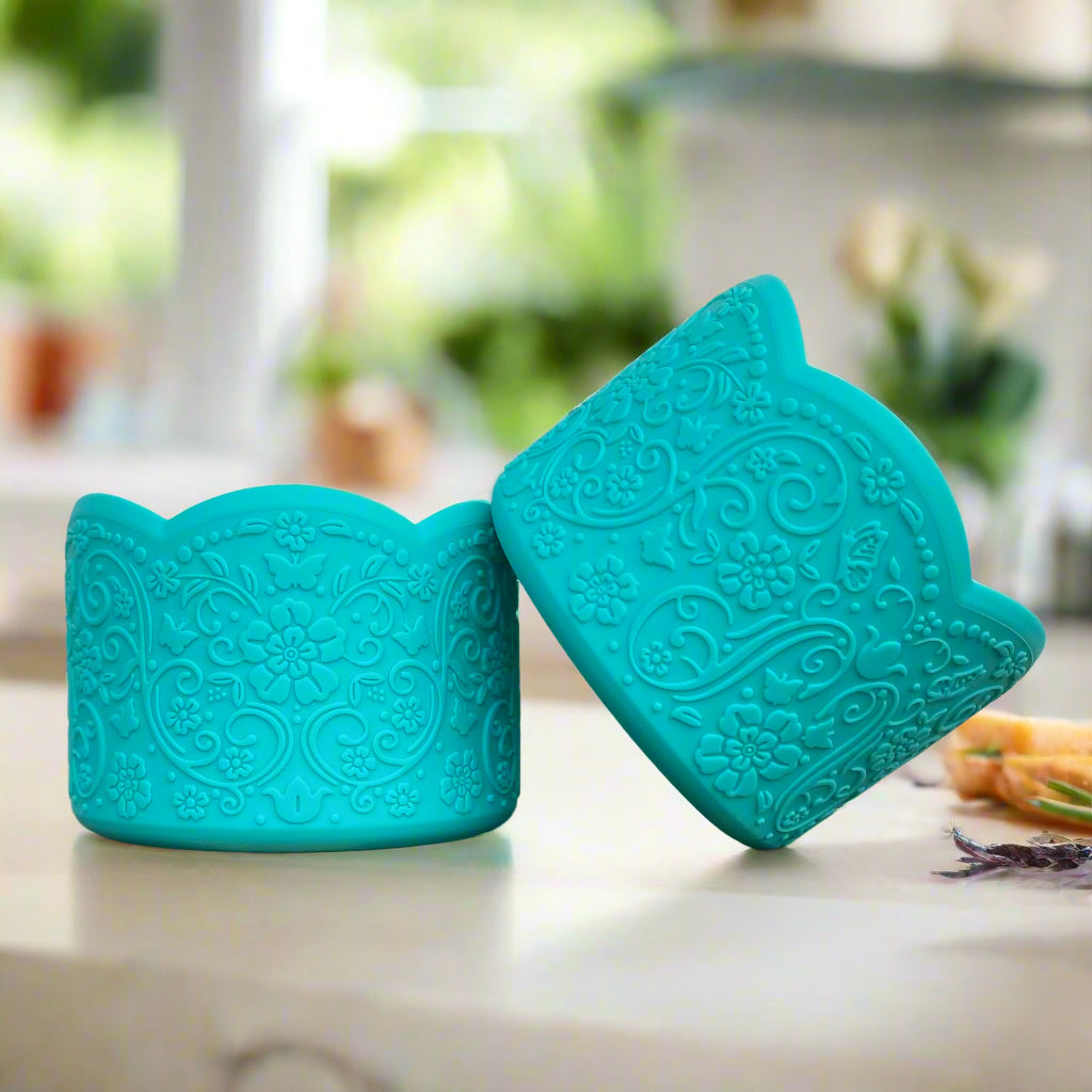 Kelsey LUXE Tumbler Boot – A vintage-inspired silicone tumbler boot featuring an intricate 3D floral design with a delicate scalloped edge. Designed to fit most 20-40 oz tumblers, this unique and upscale tumbler accessory enhances style while helping protect the base. Shown in a Tiffany Blue hue on a marble countertop with a blurred modern kitchen background