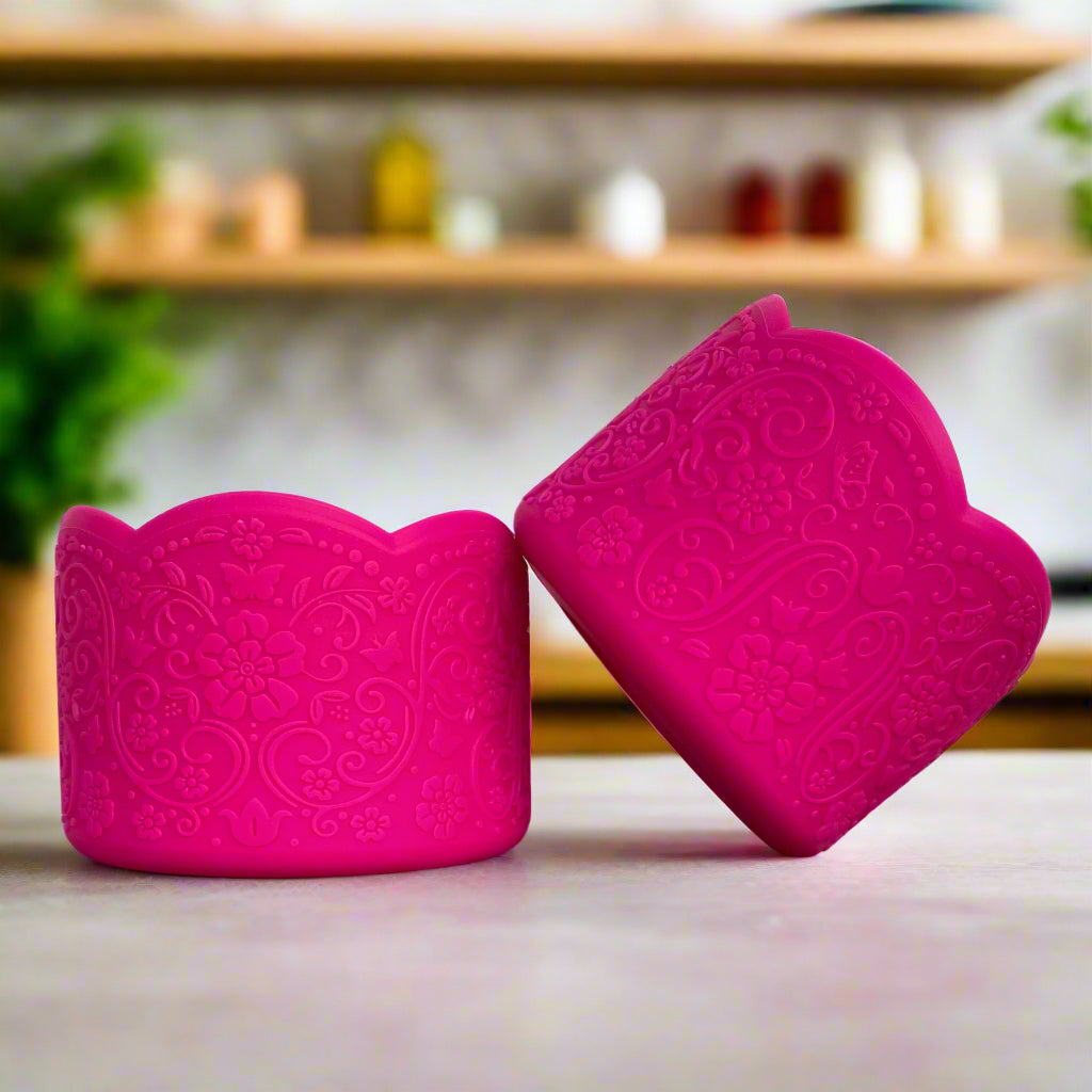 Penelope LUXE Tumbler Boot – A vintage-inspired silicone tumbler boot featuring an intricate 3D floral design with a delicate scalloped edge. Designed to fit most 20-40 oz tumblers, this vibrant and upscale tumbler accessory enhances aesthetics while helping protect the base. Shown in a bold hot pink hue on a neutral countertop with a blurred modern kitchen background.